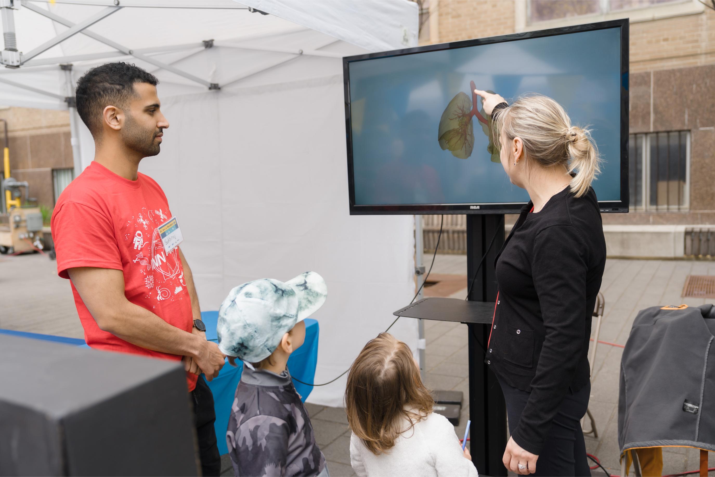 A volunteer engaging with a family of three at the Lung Function Booth.